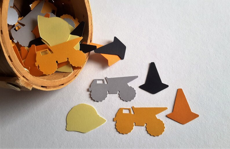 May include: A wooden bucket overflowing with construction themed paper cutouts. The cutouts include dump trucks, cones, and hard hats in yellow, orange, grey, and black.