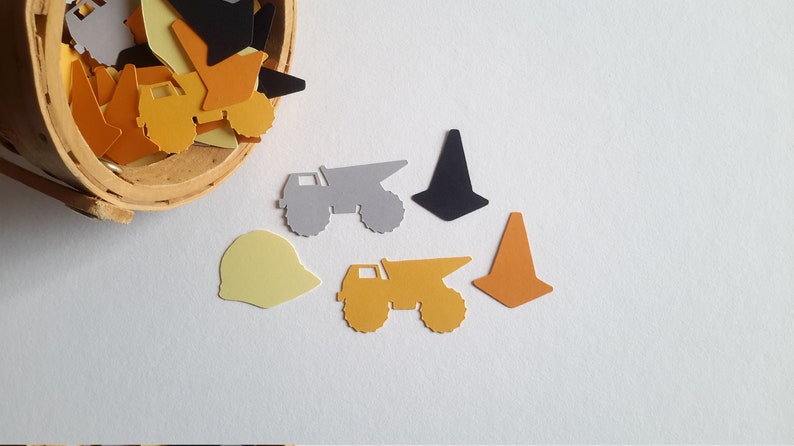 May include: A collection of construction-themed paper cutouts, including dump trucks, cones, and hard hats. The cutouts are in various colours, including yellow, orange, black, and grey.