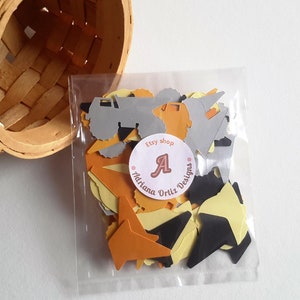 May include: A clear plastic bag filled with confetti featuring construction trucks, stars, and triangles in orange, yellow, black, and grey. The bag has a sticker with the text "Etsy shop Adriana Ortiz Designs" and a large letter "A".