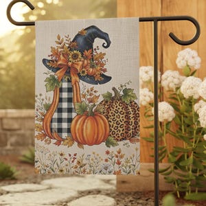 May include: A rectangular garden flag featuring a black witch hat adorned with sunflowers and autumn leaves, a tall pumpkin with a black and white buffalo check pattern, a solid orange pumpkin, and a pumpkin with a brown leopard print pattern.
