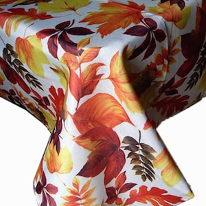 May include: A white tablecloth featuring a vibrant, repeating pattern of autumn leaves in shades of red, orange, yellow, and deep brown. The fabric displays various leaf shapes, including maple and oak, scattered across the entire surface.