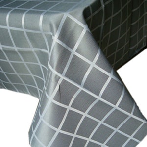May include: A gray tablecloth featuring a white grid pattern. The fabric is draped over a corner, displaying the repeating square design across the surface. The material has a subtle texture and a consistent color scheme throughout the entire piece.