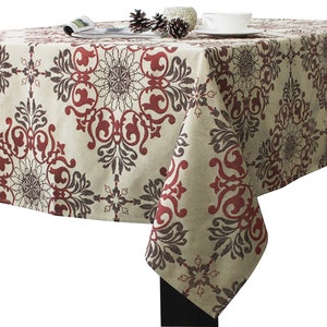May include: A rectangular tablecloth featuring a beige base color with a repeating damask pattern in deep red and dark brown. The fabric drapes over the edges of a table, displaying a symmetrical floral-inspired design across the entire surface.