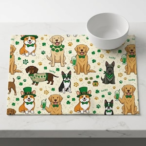 May include: A beige placemat with a repeating pattern of cartoon dogs, shamrocks, and paw prints. The dogs are wearing St. Patrick's Day attire, including green bow ties and hats. A white bowl sits on the right.