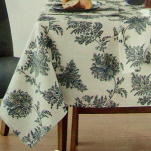 May include: A white tablecloth with a blue floral pattern. The tablecloth is made of a soft, woven fabric and has a subtle sheen. The tablecloth is laid out on a table with a wooden chair.