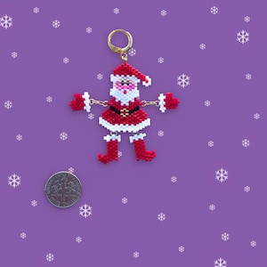 May include: A beaded Santa Claus ornament with a red and white suit, white beard, and black belt. The ornament is hanging from a gold hoop.