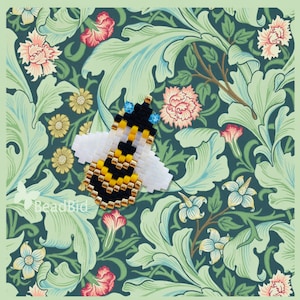 Puede incluir: Una abeja abejorro de cuentas con rayas amarillas y negras, alas blancas y detalles azules. La abeja está sobre un fondo floral verde y blanco.