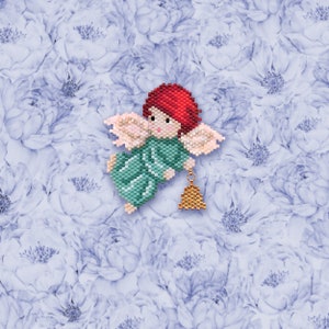 May include: A beaded angel ornament with red hair, green wings, and a gold bell. The angel is flying with its wings spread out. The ornament is on a background of blue and white flowers.
