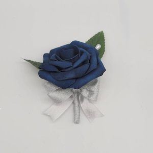 May include: A navy blue silk rose boutonniere with a silver satin bow and green leaves.