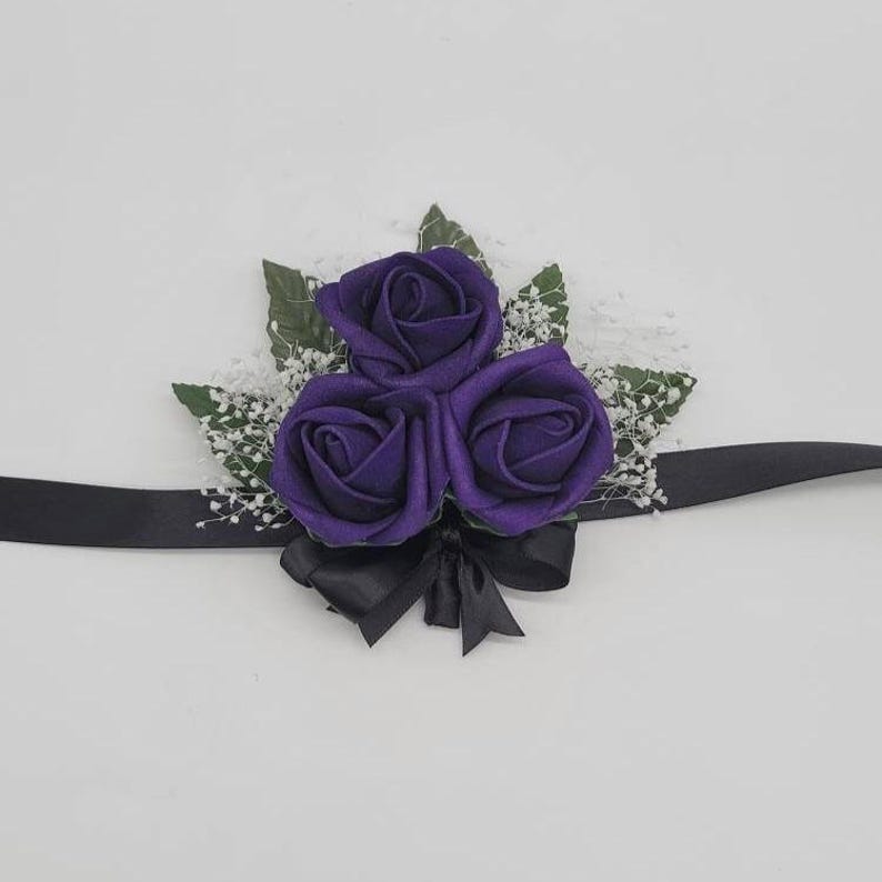 Wrist corsage in dark purple rose buds, black ribbon, 5 faux leaves and finished with baby's breath.
