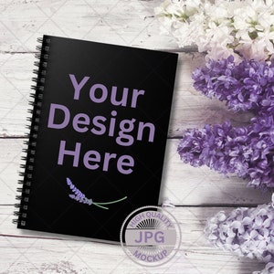 May include: Black spiral bound notebook mockup with the text "Your Design Here" on a white wood background with purple and white flowers.