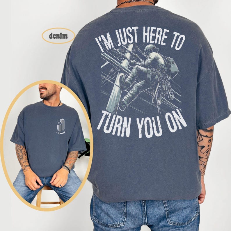 Puede incluir: Una camiseta azul oscuro con un gr&aacute;fico de un lineman escalando un poste de electricidad. El texto "I'm just here to turn you on" est&aacute; impreso en la parte posterior de la camiseta.
