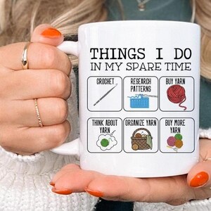 May include: White ceramic mug with a black outline and text that reads "Things I do in my spare time". The mug is divided into six squares with illustrations and text. The squares read "crochet", "research patterns", "buy yarn", "think about yarn", "organize yarn", and "buy more yarn".