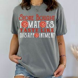May include: A grey t-shirt with the text "Store Bought Tomatoes Taste Like Disappointment" printed in white with red tomato slices.