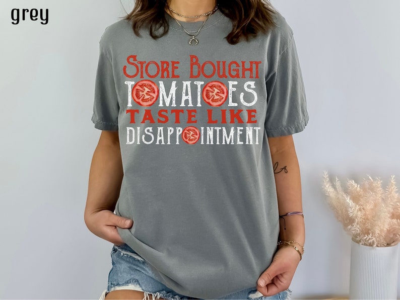 May include: A grey t-shirt with the text "Store Bought Tomatoes Taste Like Disappointment" printed in white with red tomato slices.