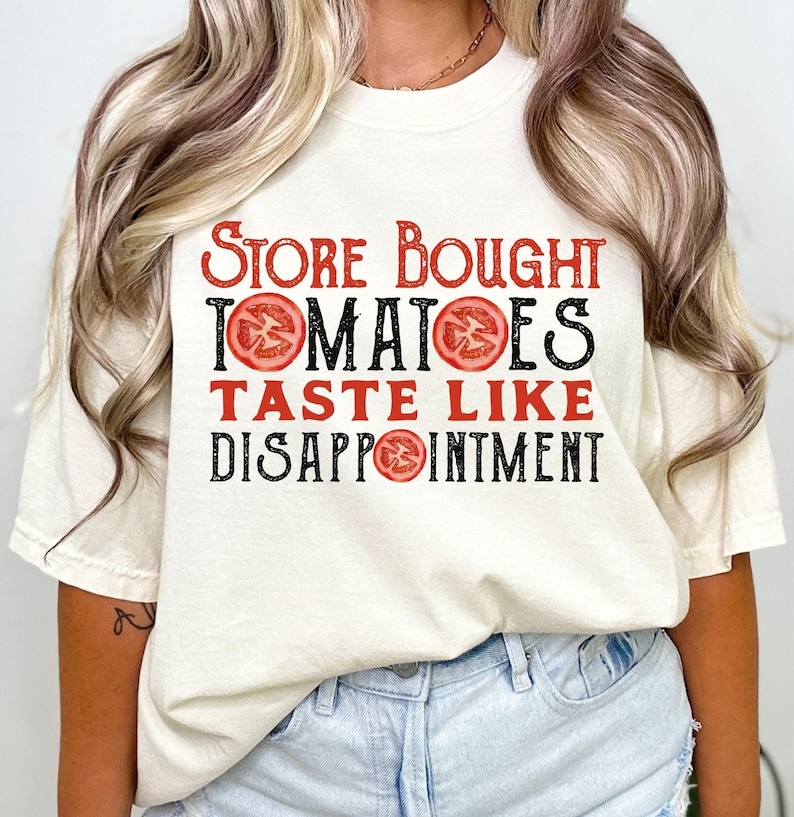 May include: White t-shirt with the text "Store Bought Tomatoes Taste Like Disappointment" in black with red tomato illustrations.