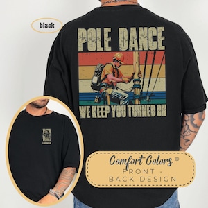 May include: Black t-shirt with a vintage-style graphic of a lineman on a pole with the text "Pole Dance We Keep You Turned On". The shirt also has the text "Comfort Colors Front - Back Design" on the bottom.