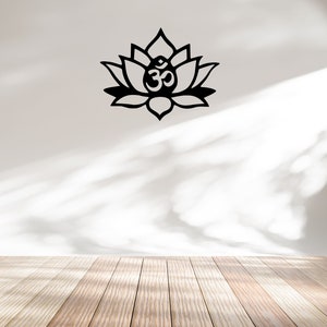 May include: A black metal wall decor featuring a lotus flower with an Om symbol in the center. The decor is mounted on a white wall with a wooden floor in the foreground.