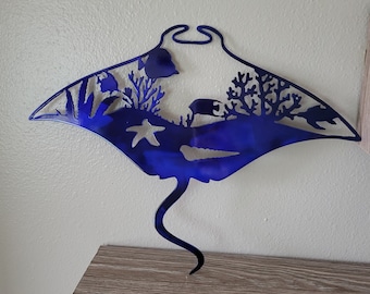 May include: A blue metal wall art sculpture of a manta ray with a starfish, coral, and fish details. The sculpture is mounted on a wooden shelf.