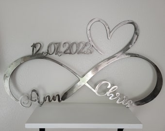 May include: Silver metal infinity symbol with a heart at the top and the names "Ann" and "Chris" on either side. The date "12.07.2023" is inscribed above the heart.