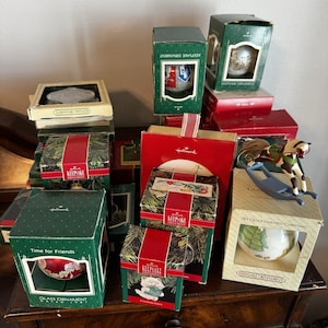 Könnte beinhalten: Eine Sammlung von Hallmark Keepsake Ornamenten in verschiedenen rechteckigen Schachteln in Grün, Rot und Creme. Auf einer Schachtel befindet sich ein Schaukelpferd-Ornament. Die Schachteln zeigen Texte wie Keepsake Ornament und Time for Friends.