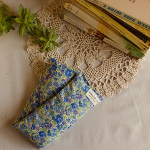May include: A yellow and blue floral print fabric eye pillow with a white label that says "Dreaming Angel Designs". The pillow is on a white crocheted doily.