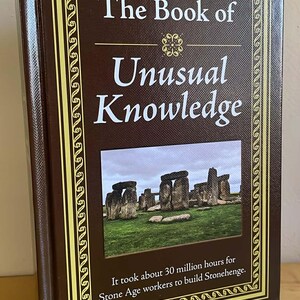 Puede incluir: Un libro de tapa dura titulado "The Book of Unusual Knowledge" con una cubierta marr&oacute;n y un borde decorativo dorado. La portada presenta una imagen de Stonehenge y el texto: "It took about 30 million hours for Stone Age workers to build Stonehenge."