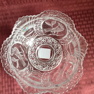 May include: A clear glass bowl with a scalloped edge and intricate etched designs of birds and floral patterns. The bowl has a sticker on the bottom.