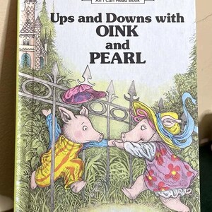 May include: A hardcover children's book titled Ups and Downs with OINK and PEARL by Kay Chorao. The cover features an illustration of two pigs in colorful clothing standing by a metal fence, with a castle in the background and An I Can Read Book text.