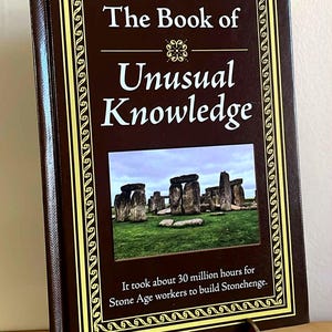Puede incluir: Un libro de tapa dura titulado "The Book of Unusual Knowledge" con una cubierta marr&oacute;n y un borde decorativo dorado. El libro presenta una imagen de Stonehenge y un texto que indica que se tardaron 30 millones de horas en construirlo.