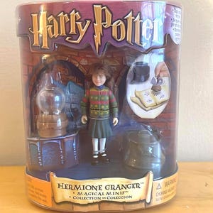 May include: A Harry Potter Hermione Granger Magical Minis Collection figure in a clear plastic package. The figure is wearing a green and red sweater and a green skirt. The packaging has the Harry Potter logo.