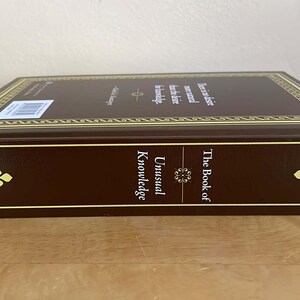 Puede incluir: Un libro de tapa dura titulado "The Book of Unusual Knowledge" en una combinaci&oacute;n de colores marr&oacute;n y dorado. El lomo del libro presenta el t&iacute;tulo y detalles florales decorativos en las esquinas. El borde superior tiene adornos dorados y texto.