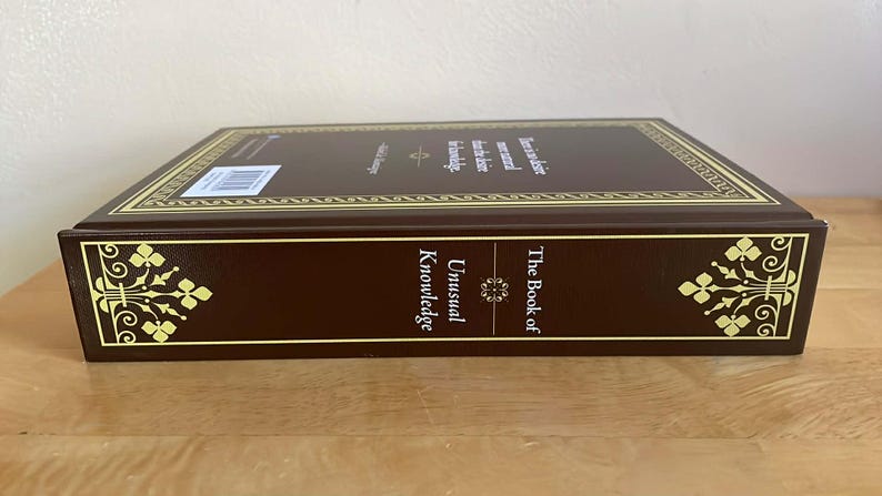 Puede incluir: Un libro de tapa dura titulado "The Book of Unusual Knowledge" en una combinaci&oacute;n de colores marr&oacute;n y dorado. El lomo del libro presenta el t&iacute;tulo y detalles florales decorativos en las esquinas. El borde superior tiene adornos dorados y texto.