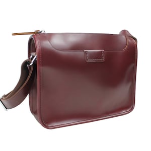 May include: A burgundy leather satchel bag with a long adjustable strap and a zipper closure.