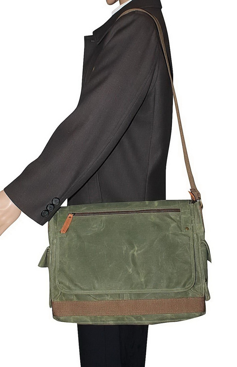 May include: A green canvas messenger bag with a brown strap and a brown accent on the bottom. The bag has a zippered pocket on the front and a flap closure.