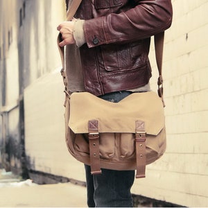 May include: A brown leather jacket with a beige canvas messenger bag. The bag has two adjustable buckles on the front flap.