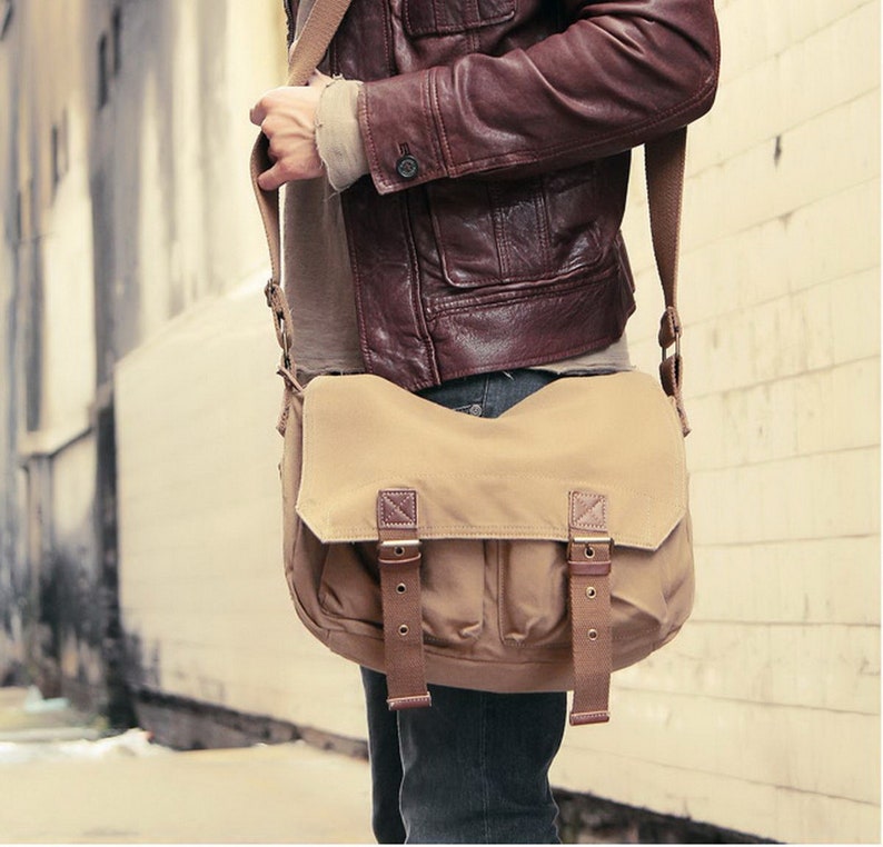 May include: A brown leather jacket with a beige canvas messenger bag. The bag has two adjustable buckles on the front flap.