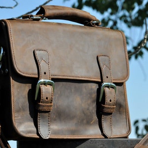 May include: A brown leather briefcase with two buckles and a long strap. The bag has a worn, distressed look.