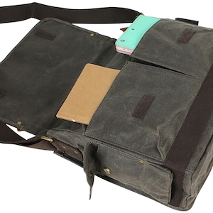 May include: A brown canvas messenger bag with a brown leather strap and a zippered pocket. The bag is open and has a notebook and a tablet inside.