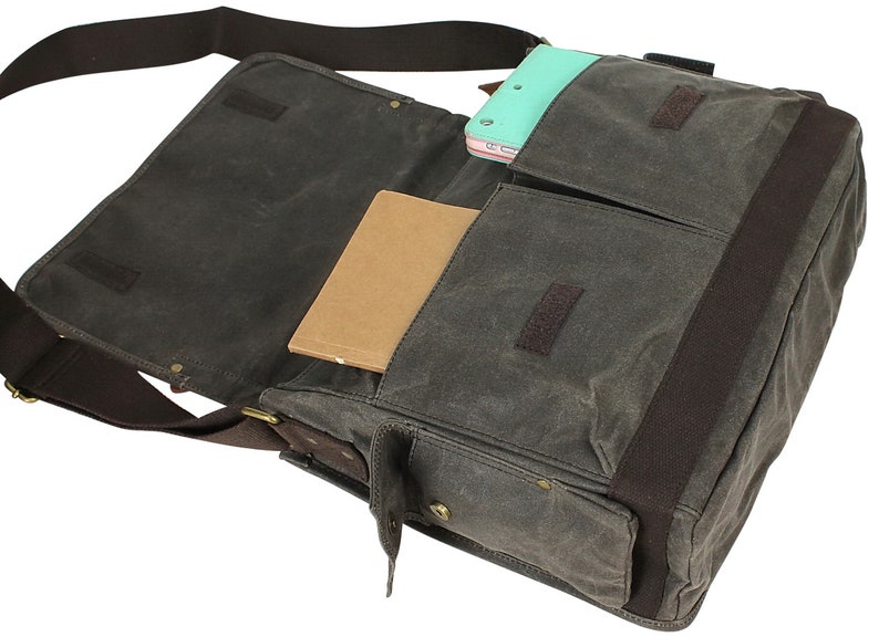May include: A brown canvas messenger bag with a brown leather strap and a zippered pocket. The bag is open and has a notebook and a tablet inside.