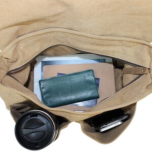 May include: A tan canvas messenger bag with a zippered top and a brown leather flap. The bag is open and contains a tablet, a notebook, a wallet, a phone, and a travel mug.
