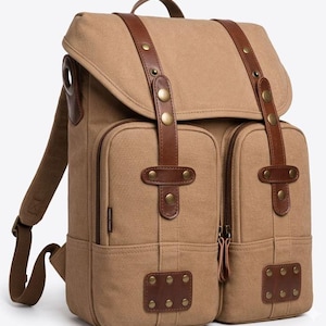 Puede incluir: Mochila de lona beige con correas y detalles de cuero marrón. La mochila tiene dos bolsillos delanteros con cremalleras, una solapa de cierre y correas ajustables para los hombros. Cuenta con herrajes metálicos de color latón.