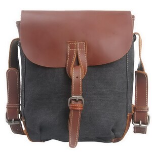 May include: A gray canvas messenger bag with a brown leather flap and straps. The bag features a buckle closure and white stitching details. The bag has adjustable shoulder straps and is designed for carrying items.