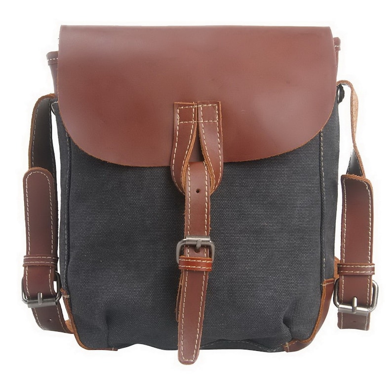 May include: A gray canvas messenger bag with a brown leather flap and straps. The bag features a buckle closure and white stitching details. The bag has adjustable shoulder straps and is designed for carrying items.
