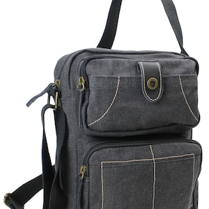May include: A black canvas messenger bag with multiple pockets and a flap closure. The bag has a brown leather strap and a zippered pocket on the front.