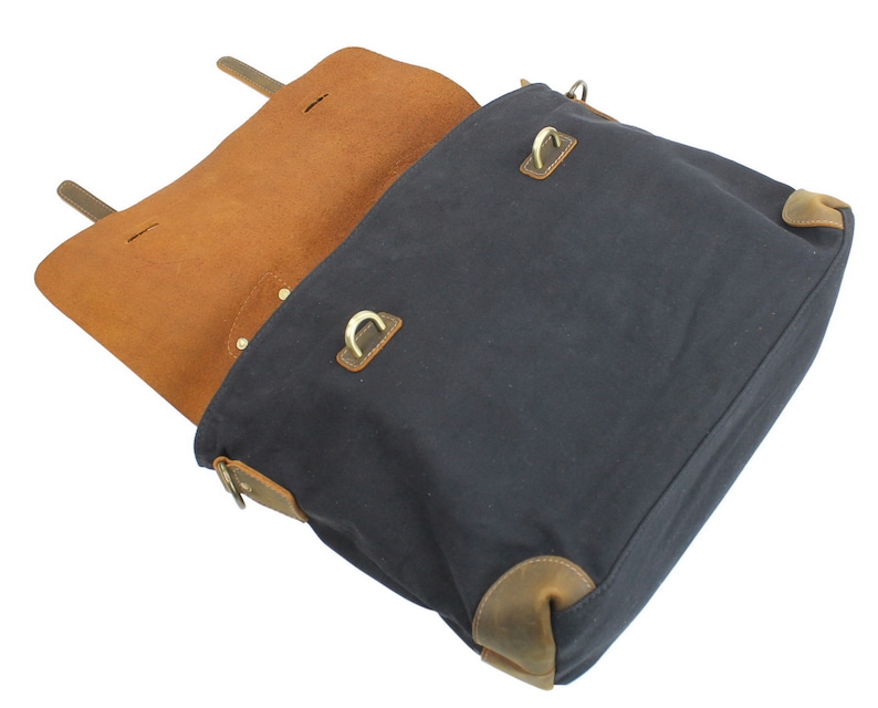 May include: A dark blue canvas messenger bag with brown leather accents and brass hardware. The bag is open and the inside is lined with brown leather.