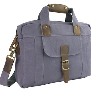 Puede incluir: Un bolso de mensajero de lona gris con detalles de cuero marrón y cierre de hebilla. El bolso tiene un asa superior y una correa para el hombro.