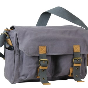 May include: A gray canvas messenger bag with brown leather accents and two adjustable buckles. The bag has a front pocket and a zippered closure.