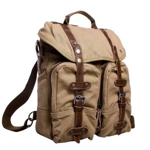 May include: A tan canvas backpack with brown leather straps and buckles. The backpack has two large front pockets and a smaller pocket on the side.
