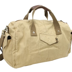 May include: A beige canvas duffel bag with brown leather handles and a shoulder strap. The bag has a large front pocket and a smaller pocket on the side.